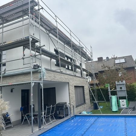 Gerüst an einer modernen Einfamilienhausfassade mit Pool im Vordergrund.