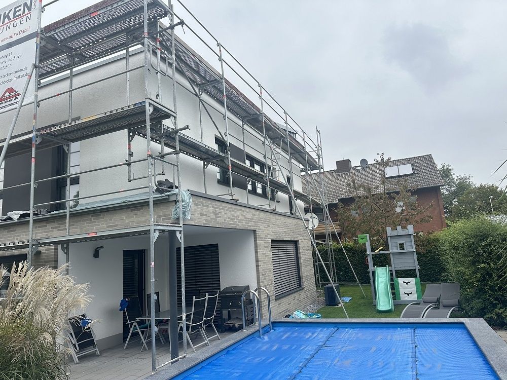 Gerüst an einer modernen Einfamilienhausfassade mit Pool im Vordergrund.
